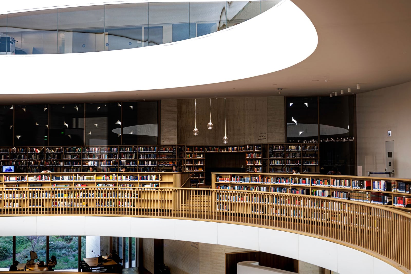 Interior de biblioteca pública moderna, con balconadas curvas de madera a varios niveles y un gran lucernario que deja entrar luz natural