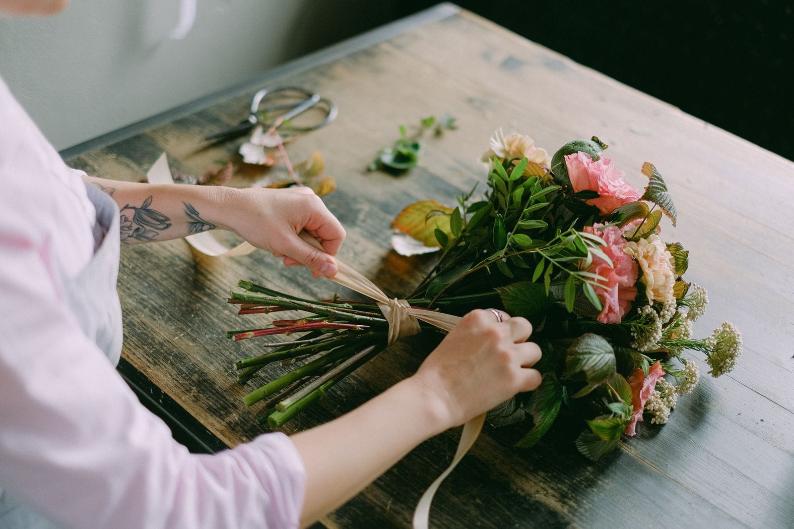 Florista componiendo un ramo de temporada sobre la mesa de trabajo del taller